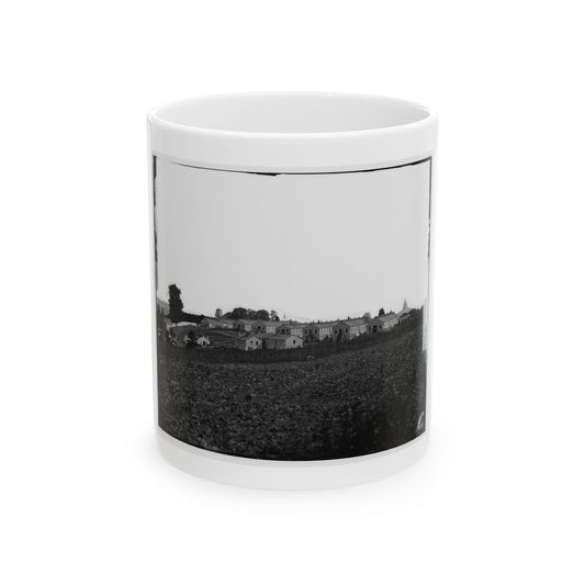 Black and white 1860s view of long wooden barracks on a rise above a ploughed field, with a water tower.