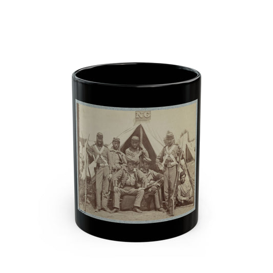 Sepia print showing seven soldiers with rifles posed in front of a canvas tent, some seated on a log.