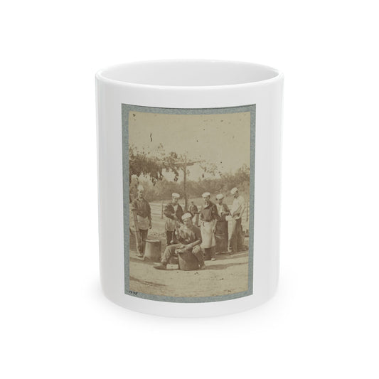 Sepia print showing six men in white caps and aprons standing around metal kettles at an outdoor camp kitchen.
