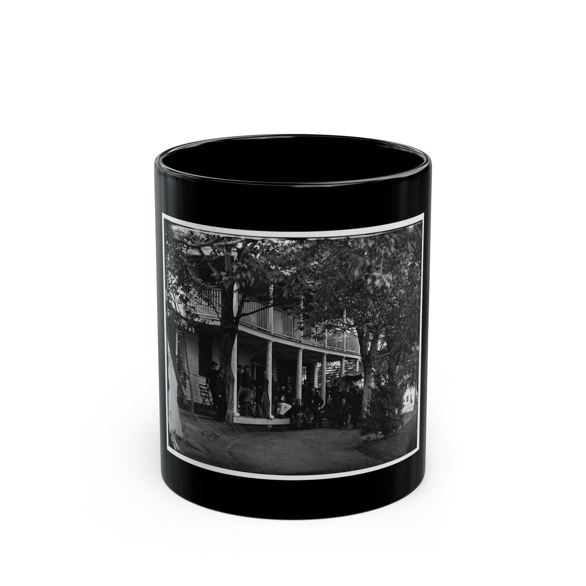 Black and white view of uniformed men gathered on the porch of a two-story wooden building beneath trees.