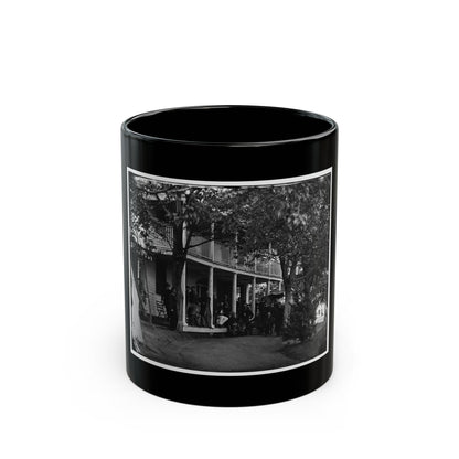 Black and white view of uniformed men gathered on the porch of a two-story wooden building beneath trees.