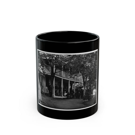Black and white view of uniformed men gathered on the porch of a two-story wooden building beneath trees.