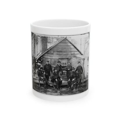 Black-and-white 1860s group view of eight officers in dark uniforms posed outside a log cabin.