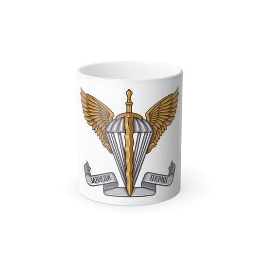 Military emblem with a silver parachute and gold wavy dagger between feathered wings, with a banner below.