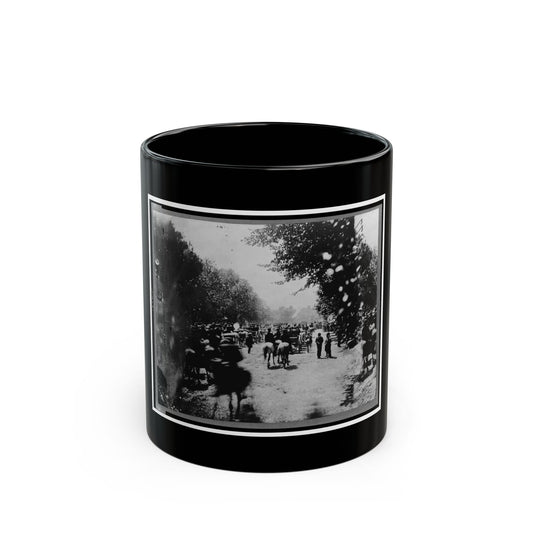 Black and white view of a blurred crowd of mounted riders and wagons on a tree-lined dirt road.