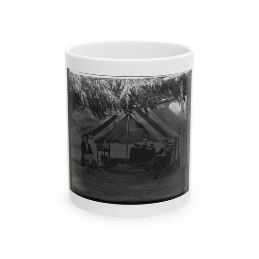 Black and white camp scene of two men seated outside a canvas tent under overhanging trees, with a camp table.