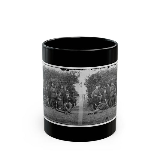 Black-and-white stereo view of uniformed men posed in a group outdoors in front of a leafy shrub.
