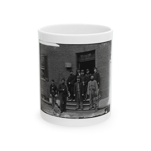 Monochrome historical scene of uniformed men on the steps of a brick building, with a seated child in front.