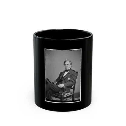 Black and white studio portrait of a seated man in a dark suit and cravat, legs crossed in a carved armchair.