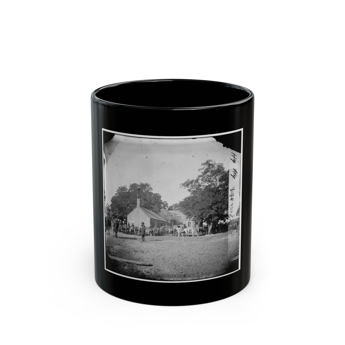Black-and-white view of mounted riders and horses gathered before a brick building under large shade trees.