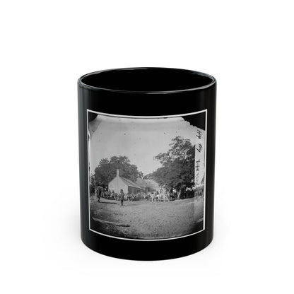 Black-and-white view of mounted riders and horses gathered before a brick building under large shade trees.