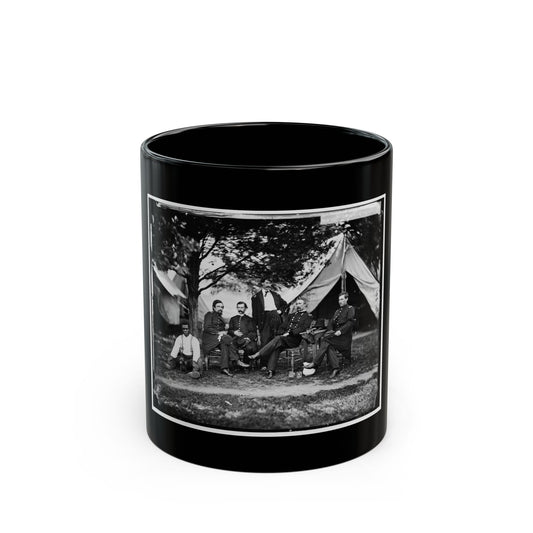 Black and white group view of six men before a canvas tent under a tree, one seated with a small dog.
