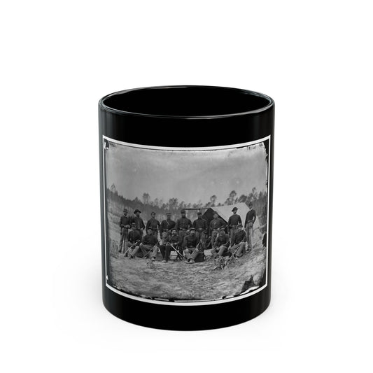 Black and white view of fifteen uniformed soldiers posed with sabers before a canvas tent in a wooded camp.