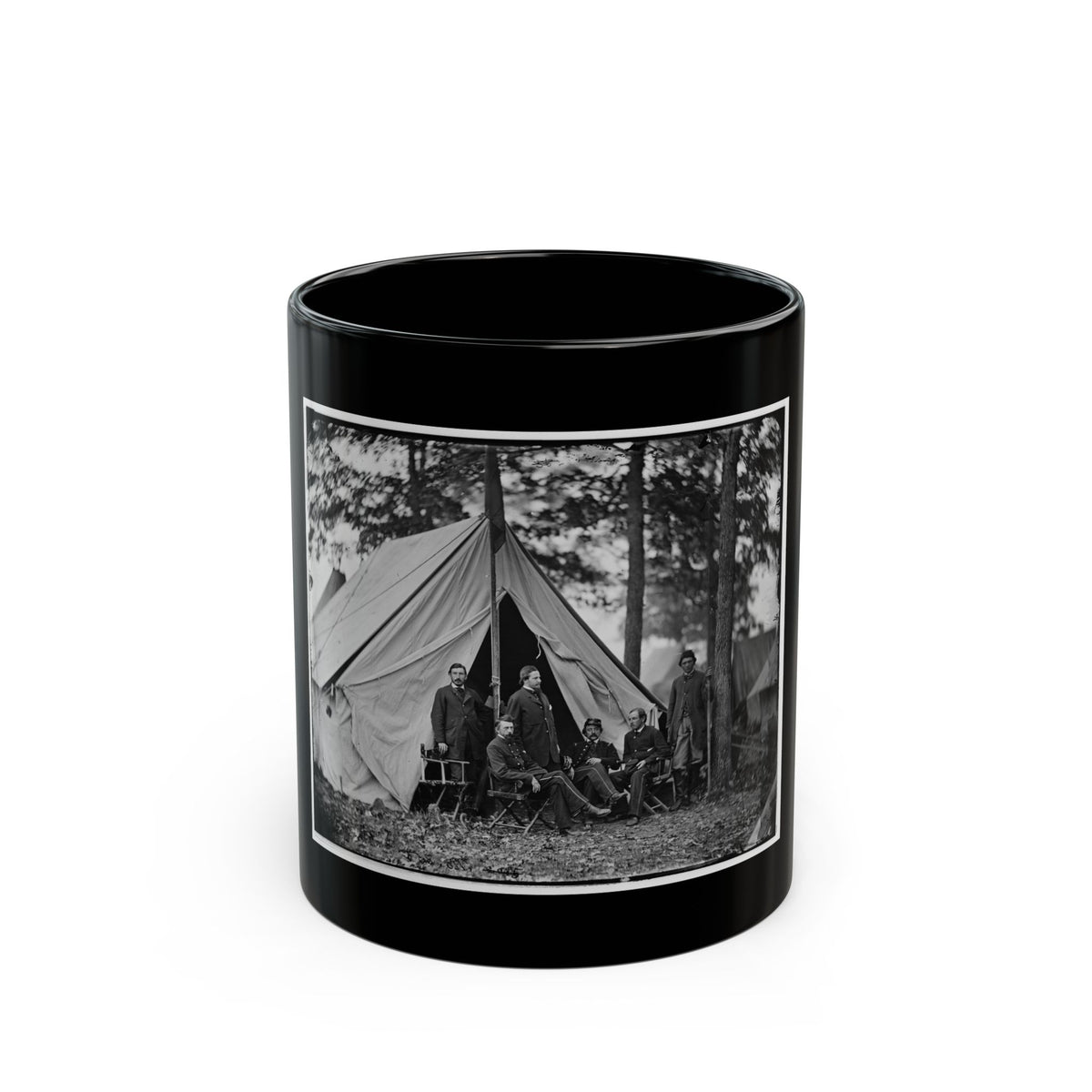 Black and white view of six men in dark coats posed before a canvas tent among tall pine trees.