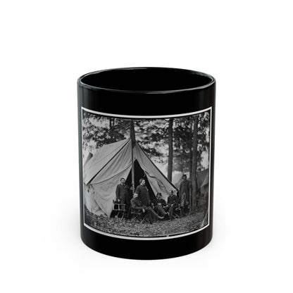 Black and white view of six men in dark coats posed before a canvas tent among tall pine trees.