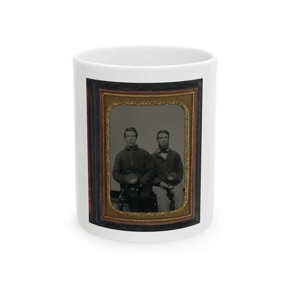 Two seated men in dark jackets holding kepi caps, in a vintage tintype portrait framed in gold diamond-pattern metal.