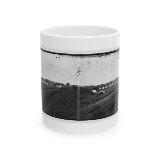 Black and white stereo view of a row of conical tents in a field beside earthworks and a dirt road.