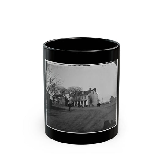 Black and white view of a two-storey historic house with a columned porch and small figures on a dirt street.