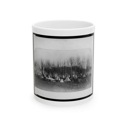 Black and white scene of a camp of conical canvas tents among bare trees, with people standing in front.