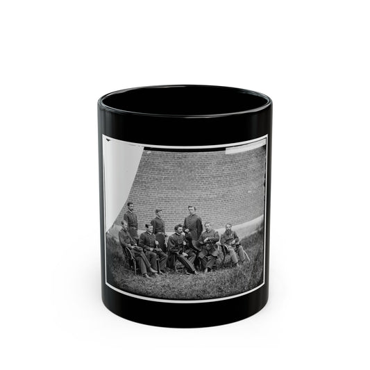 Black and white 1860s group portrait of seven uniformed officers posed on grass before a brick wall.