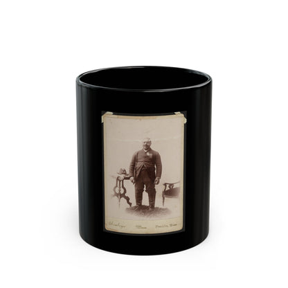 Sepia 1880s studio portrait of a standing man in a dark suit beside a carved side table holding a hat.
