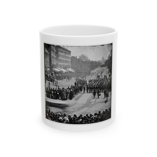 Black and white 19th-century view of a column of soldiers with rifles marching down a city avenue past crowds.