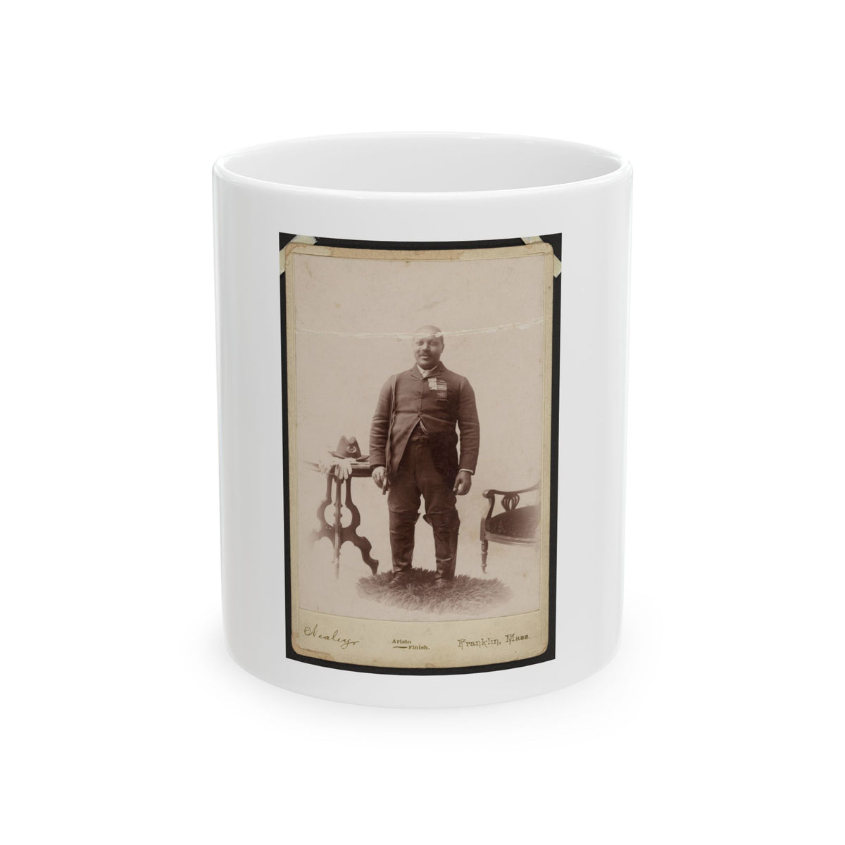 Sepia 1880s studio portrait of a standing man in a dark suit beside a carved side table holding a hat.