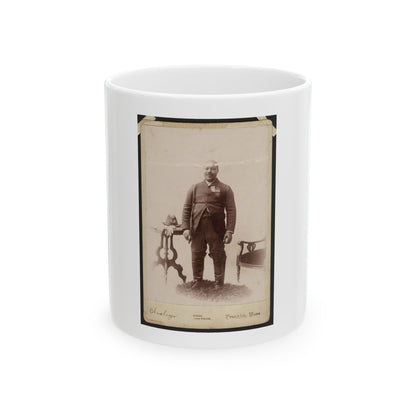 Sepia 1880s studio portrait of a standing man in a dark suit beside a carved side table holding a hat.