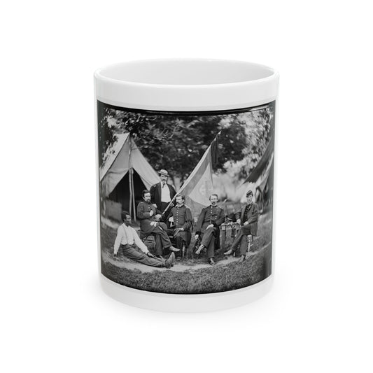 Black and white 1860s group portrait of six men in military uniforms posed outdoors by white tents, with a flag on a pole.